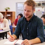 Un apprenant adulte écrit dans son cahier pendant une dictée en classe de français